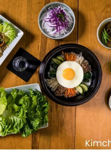 korean Bibimbap (Korean Mixed Rice with Meat and Assorted Vegetables) in a ceramic bowl , a water of glass, a Champaign bottle, some korean salids are placing on a wooden table