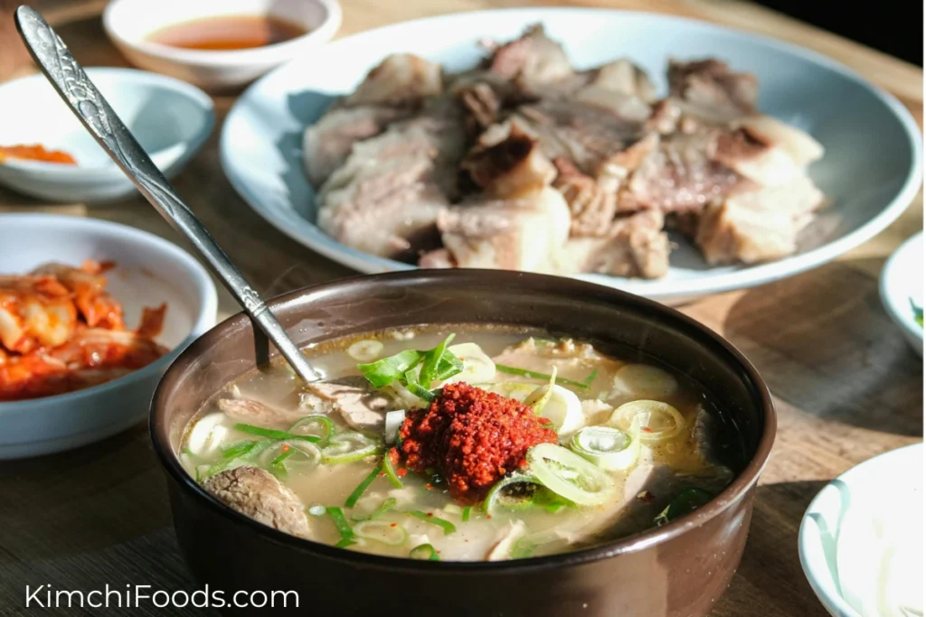 there is a kimchi pork soup in a ceramic bowl placed on the table