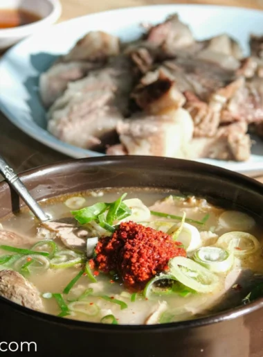 there is a kimchi pork soup in a ceramic bowl placed on the table