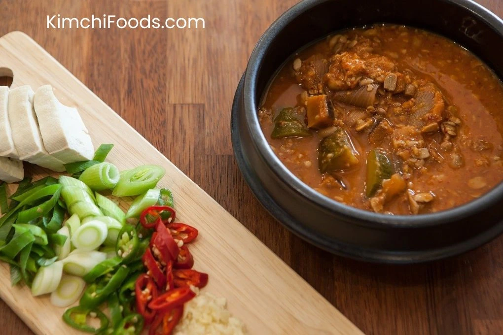 a bowl full of Kimchi jjigae (kimchi stew) placing on the wooden table along with chilies and garlic