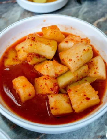 Korean Radish Kimchi (Kkakdugi) in a white ceremic bowl placing on a wooden table