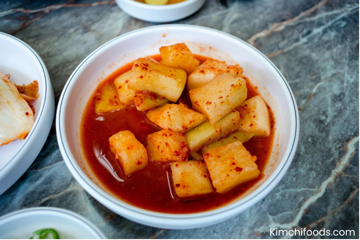 Korean Radish Kimchi (Kkakdugi) in a white ceremic bowl placing on a wooden table